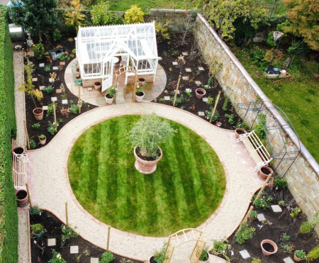 Aerial view of a landscaped garden with a circular lawn, gravel path and greenhouse