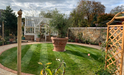 Landscaped garden with circular lawn, gravel path and greenhouse